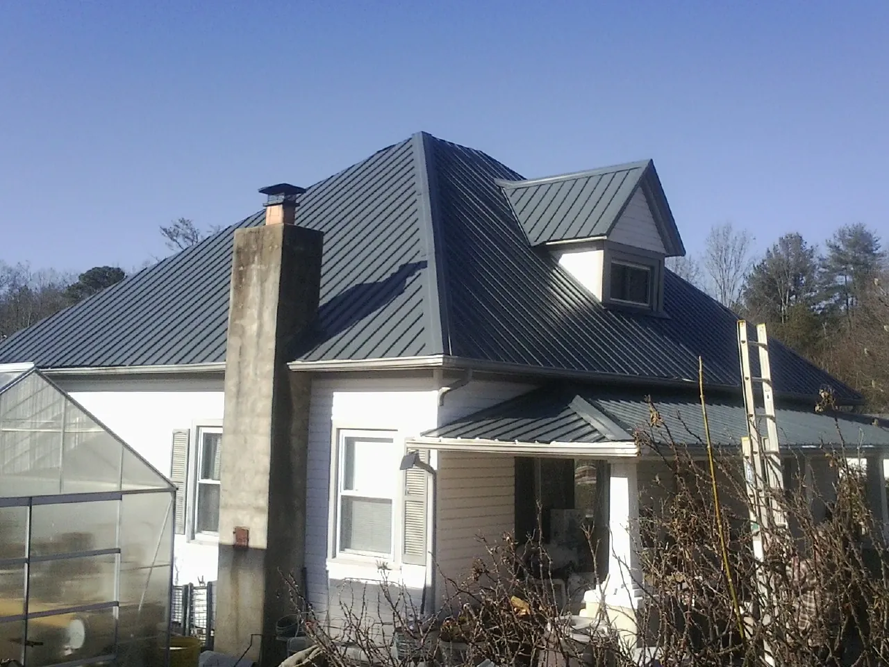 Dark blue standing seam metal roof on a white farmhouse with dormer — Slate & Tile Roof Repair by Roofing Brothers in Coin