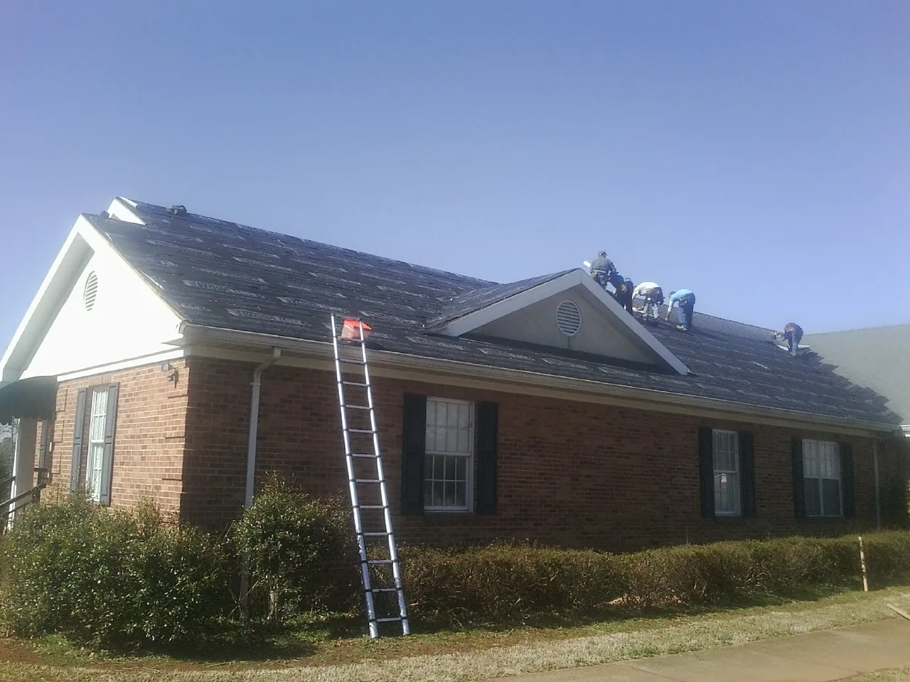 Crew tearing shingles off a brick ranch roof with a ladder set — Emergency Roof Repair work by our crew in Coin