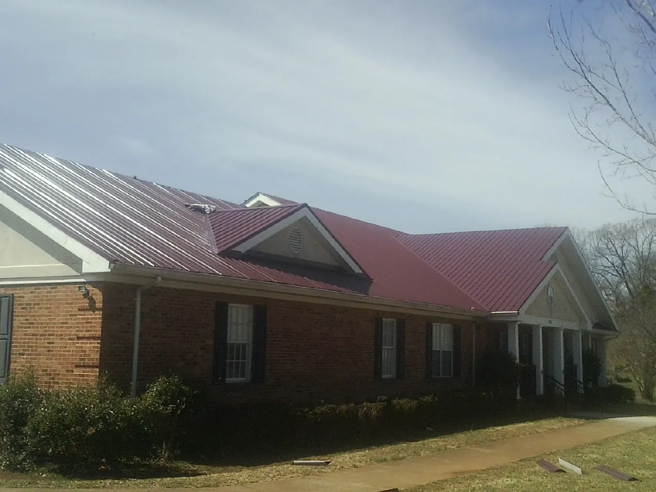 Red metal roof with gabled entries on a long brick building, from a Hail Damage Roof Repair job in Coin