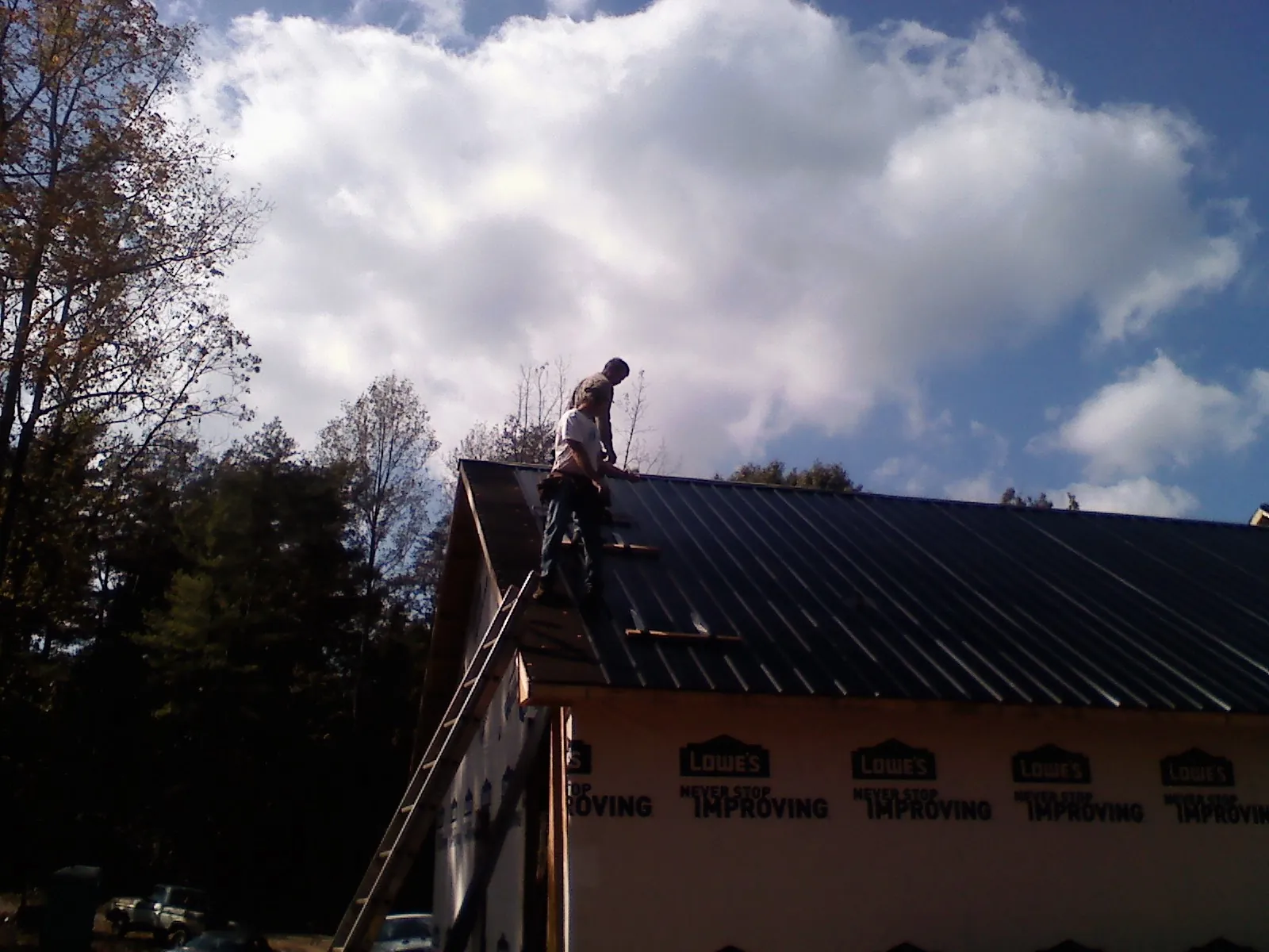 Roofer fastening dark metal panels high against a cloudy sky, from a Roof Inspection job in Coin