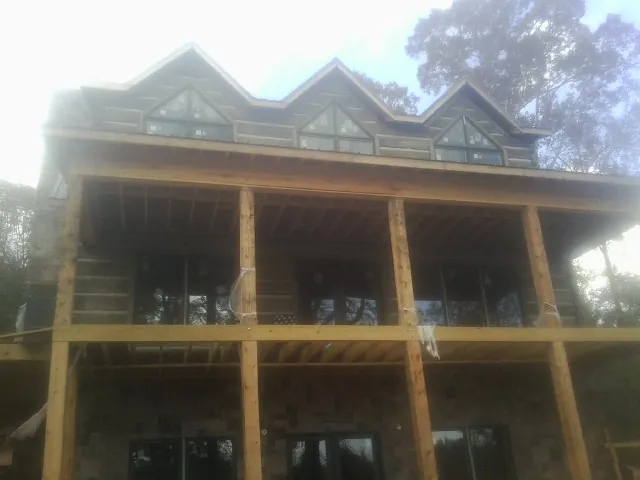 Dormers and porch framing on a large log home under construction — Roof Coating work by our crew in Coin