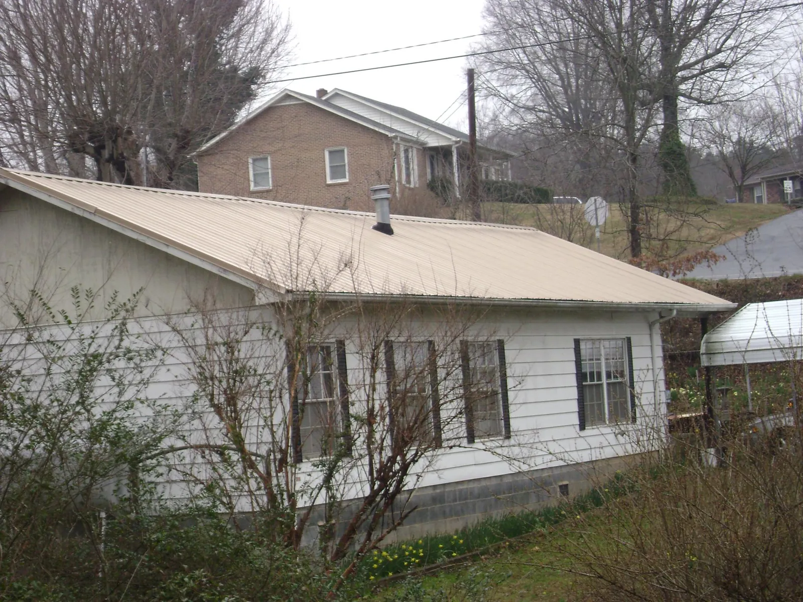 Tan metal roof on a white sided house set into a hillside — Commercial Roofing by Roofing Brothers in Coin