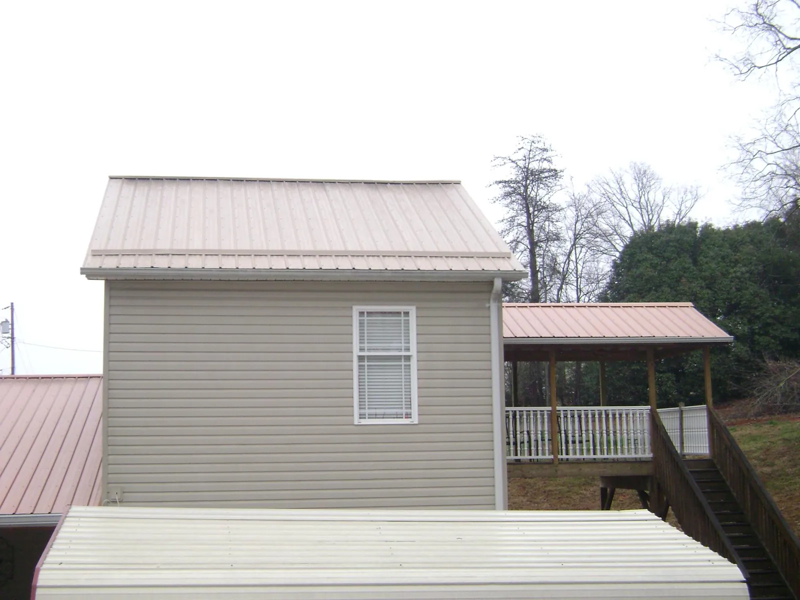 Tan metal roofs on a two story addition and attached porch, from a Roof Replacement job in Coin